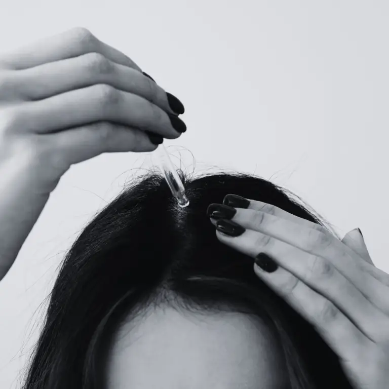 a close up image of woman putting oil hair drops on the scalp as part of healthy hair practices